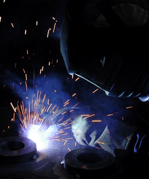 A welder wearing a helmet doing welding on a pipe