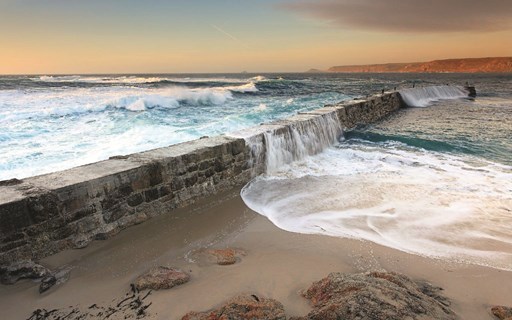 Picture of a sea wall with water spilling over the top on to the beach