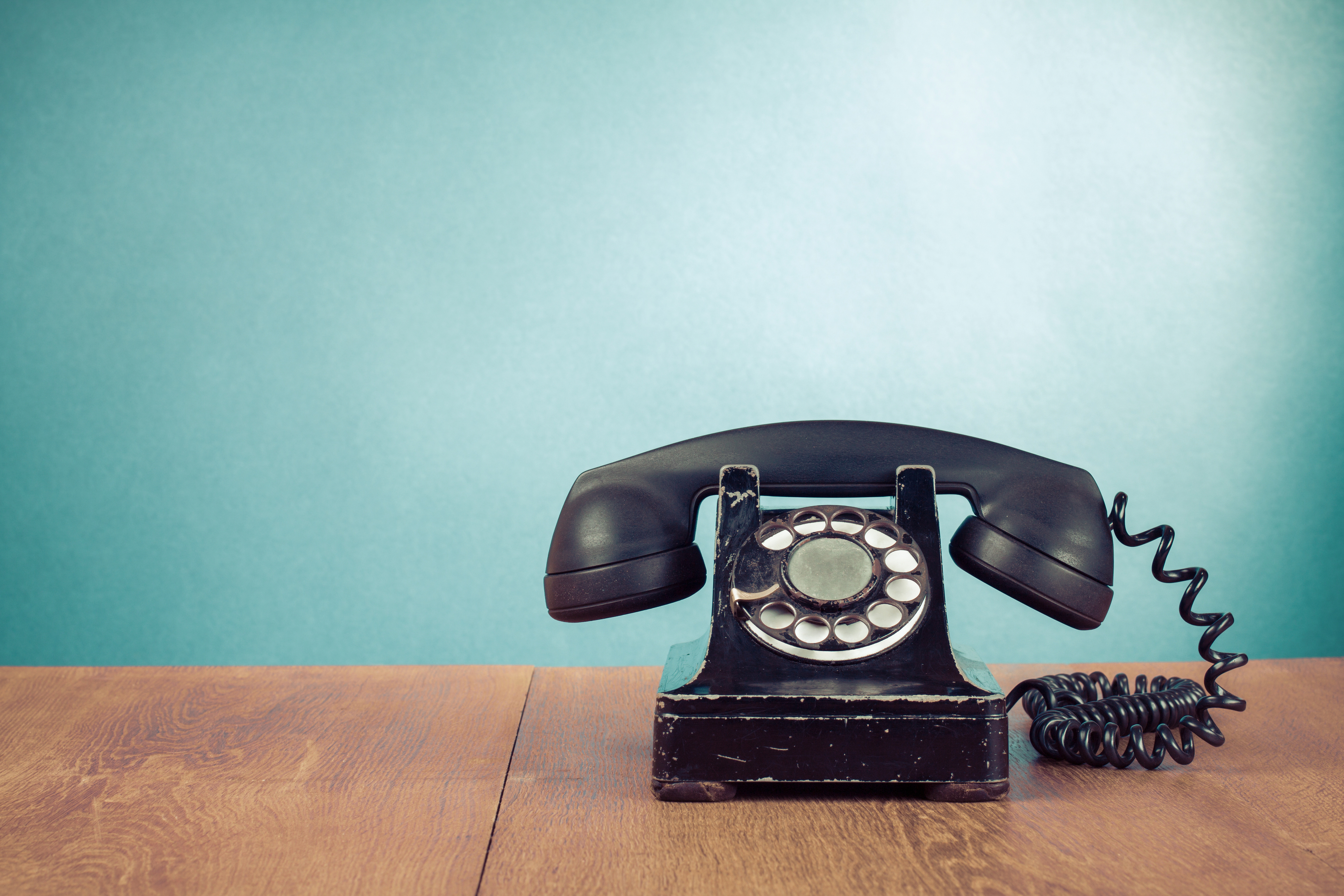 Image of old style black telephone on desk against a green background