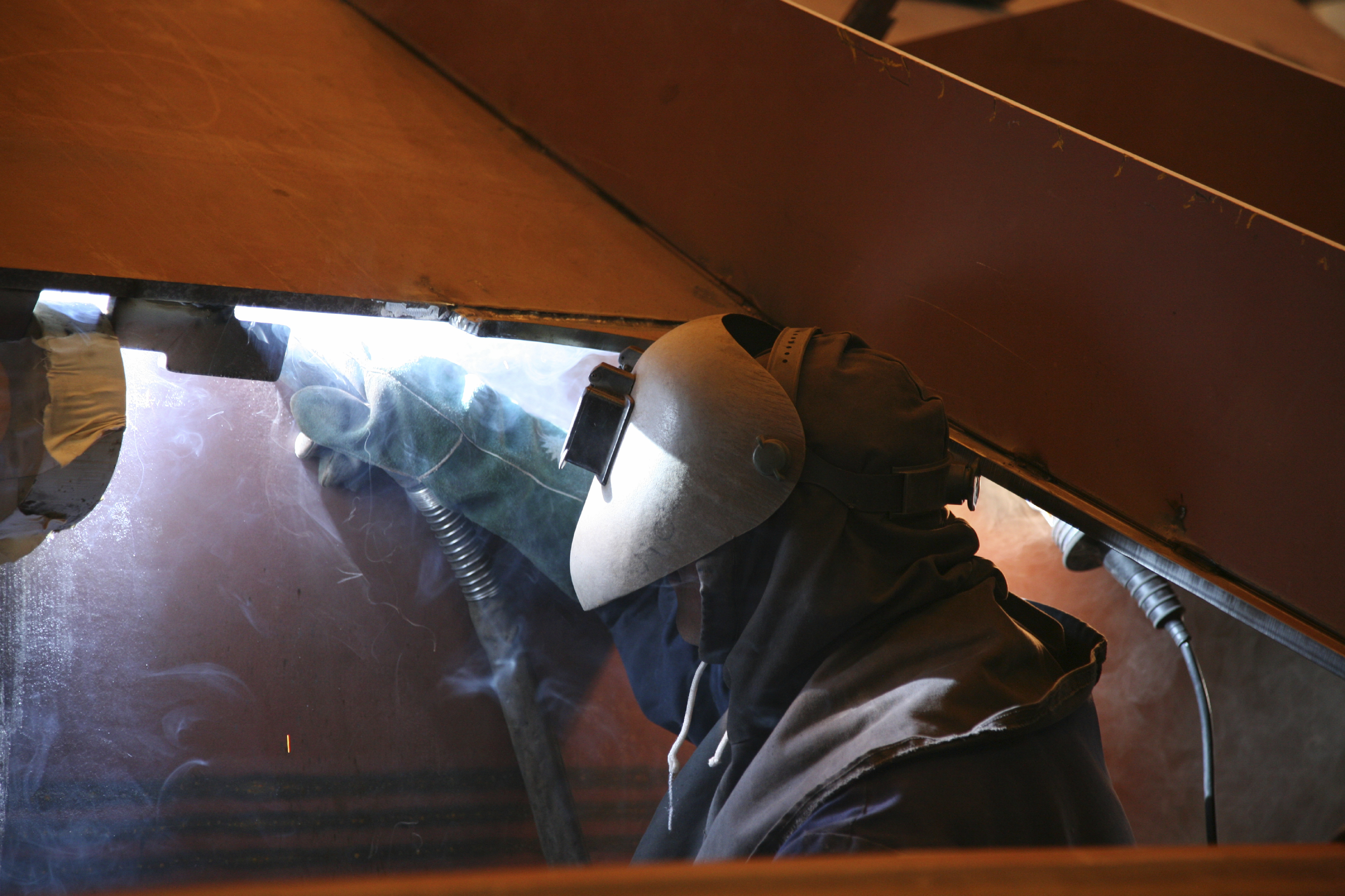 An image of a welder welding steel on the underside of a vessel