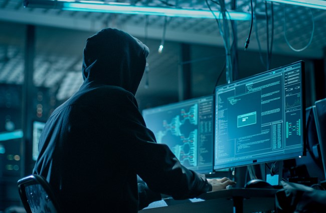 A hacker sitting at a computer looking at the screens