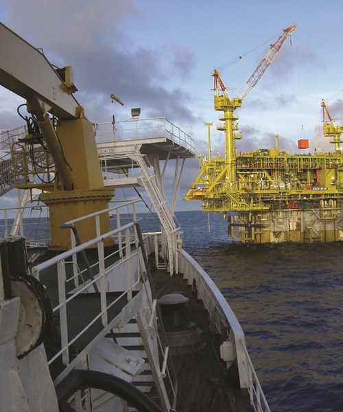 An image of an offshore oil and gas platform at sea with a vessel bow in the foreground