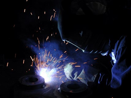 A welder wearing a helmet doing welding on a pipe
