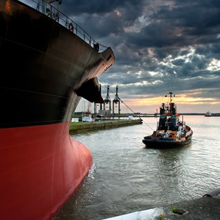 An image of a tug guiding a larger ship out of a port