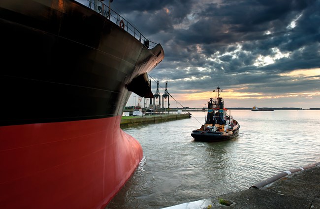 An image of a tug guiding a larger ship out of a port