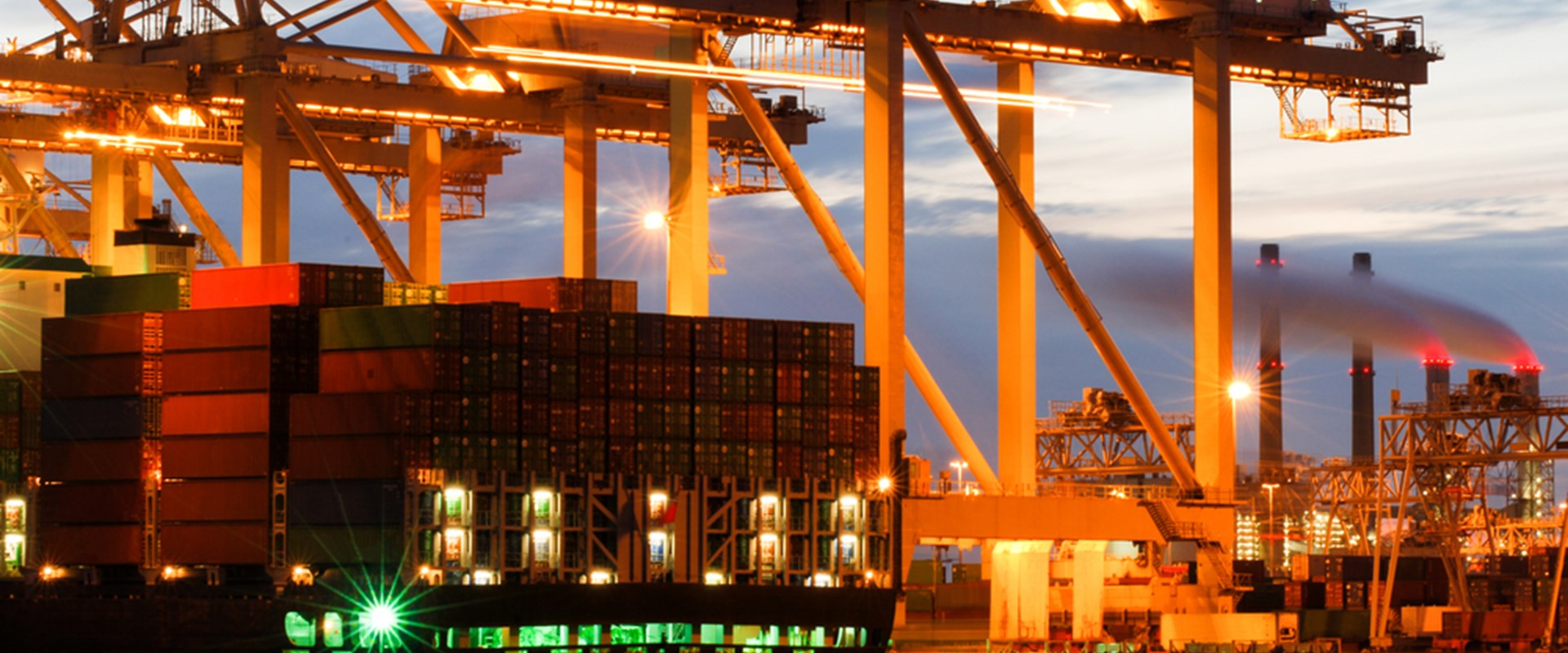 An image of a container vessel docked in a port in the evening