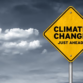 A yellow warning sign with the words 'Climate change just ahead' in front of a cloudy sky 