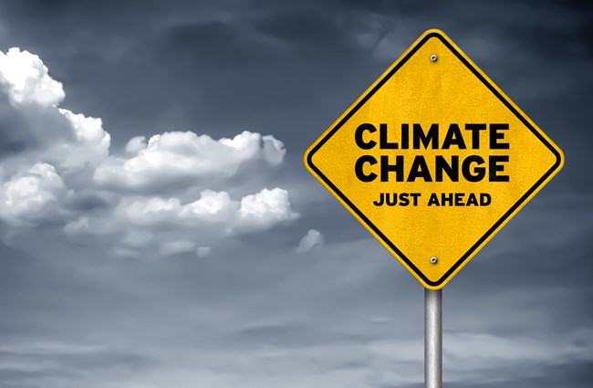 A yellow warning sign with the words 'Climate change just ahead' in front of a cloudy sky 